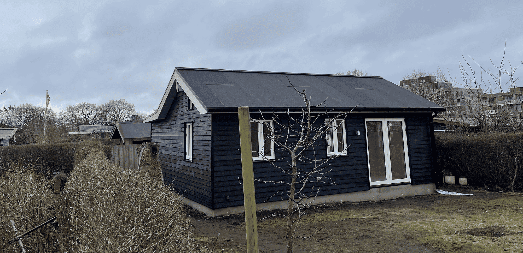 klassisk kolonihavehus i sortmalet træ med store vinduer