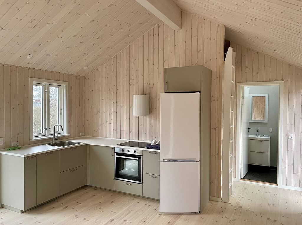 Nybygget køkken med moderne skabe, integreret ovn og køleskab i lys stue med trævægge og lofter