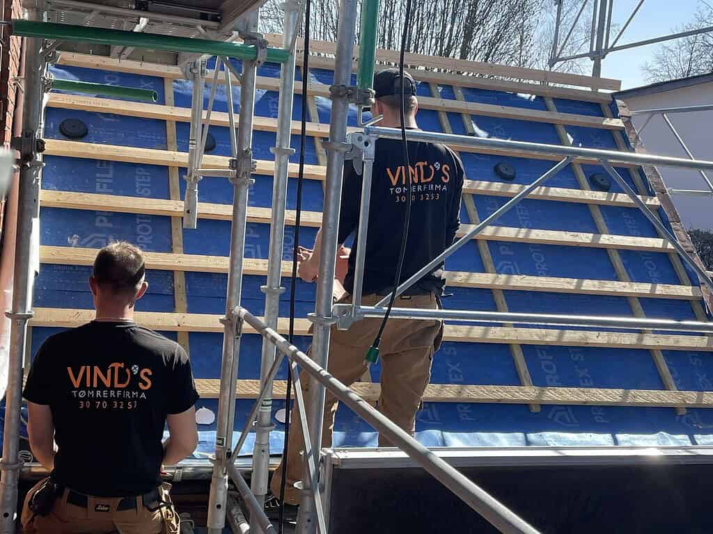 To tømrere fra vinds tømrerfirma arbejder på tagkonstruktion med træspær og tagfolie.